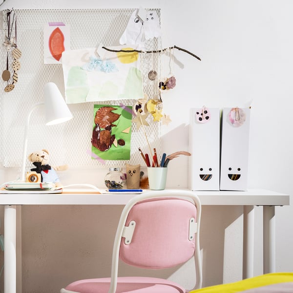Childs desk with pink chair, white TJABBA magazine files, colourful art, lamp, and supplies.