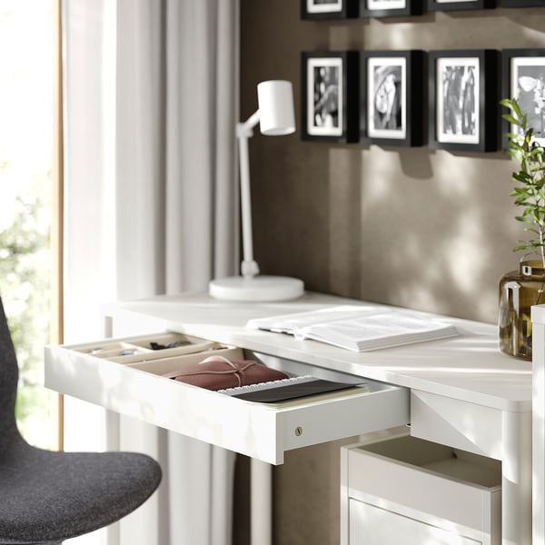 Desk with open drawer holding files, notebook, and pen near window.