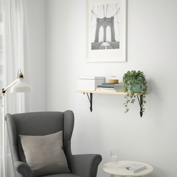 Minimalist corner with grey armchair, TRANHULT shelf, books, plant, and bridge sketch.