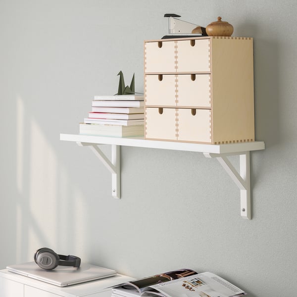 A wall-mounted shelf with drawers and brackets holding books and decor.