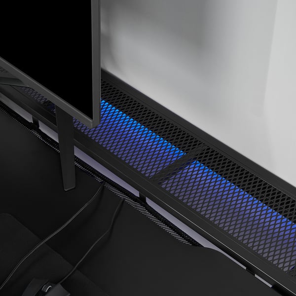 Black gaming desk with blue lighting under mesh, supporting monitor and pc, showcasing adjustable height legs and cable management.