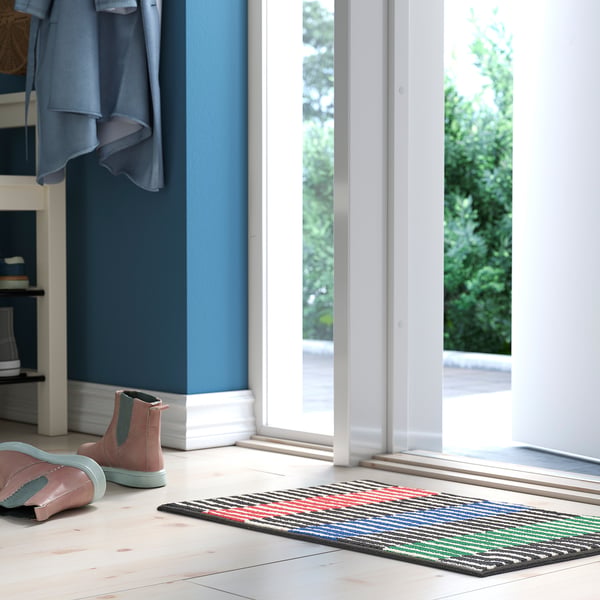 VÄNDPLATS striped mat near entrance door, pink boots, blue wall, white floor.