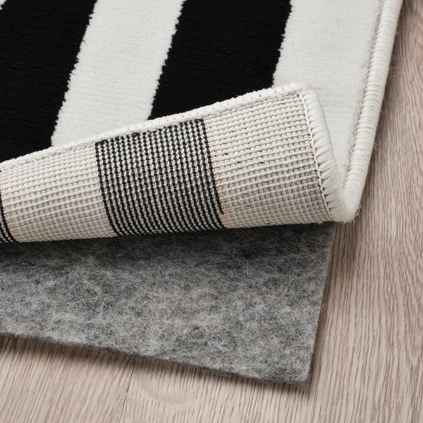 Black and white striped rug with non-slip underlay on wooden floor. Rug edge visible, showing checked pattern.