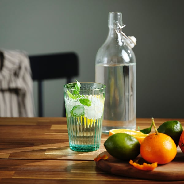 A glass of water with ice and mint, next to fruit and a bottle.