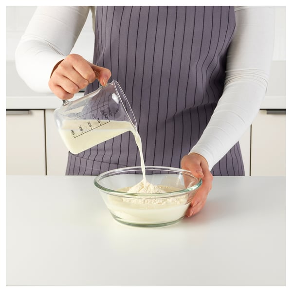 Person pours liquid from a measuring jug into a bowl of flour. The jugs markings indicate precise measurement levels.
