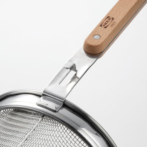 Close-up of a sturdy kitchen strainer with a wooden handle by IKEA, showing its robust design and.