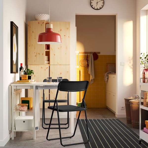 Black folding chairs and extendable white table in compact dining space.