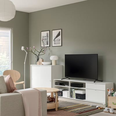 Modern living room with VIHALS storage, white tv bench, chair, green walls, photos, lamp, and vase.