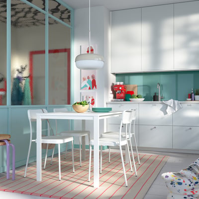 Modern kitchen with white VIHALS table and chairs, turquoise cabinets, red accents, and striped rug.