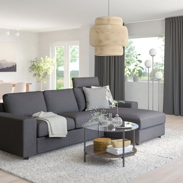 Modern living room with grey VIMLE sofa, glass table, white rug, basket, and large windows.