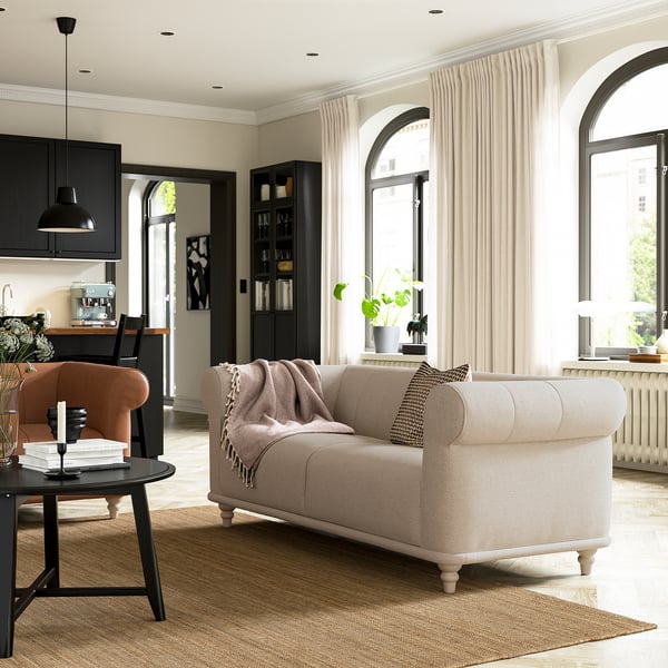 Modern living room a white VISKAFORS sofa, orange chair, black accessories, and large arched windows with sheer curtains.