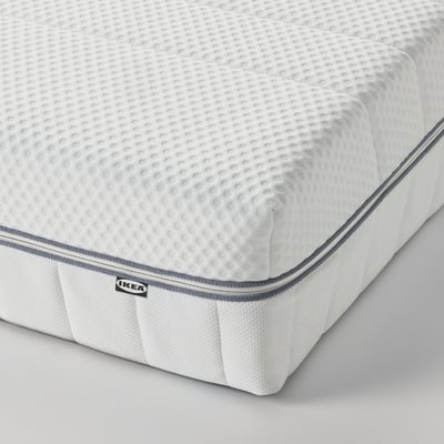 A close-up of a neatly made bed with a white mattress, featuring a textured fabric surface and a dark grey piping border.