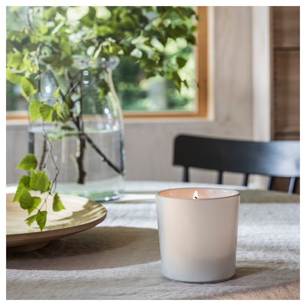 Lit candle & vase with leaves on table runner in calm interior. Alternative: lit candle, vase with leaves on textured runner, calm interior.