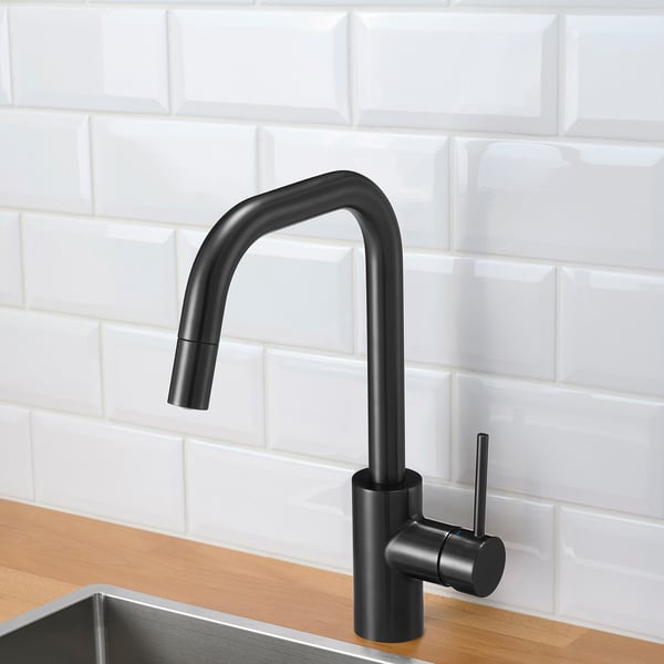 Black kitchen tap with pull-out sprayer, mounted on wood countertop against white tiled backsplash.