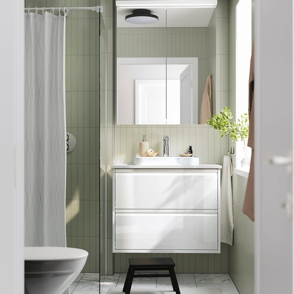 Modern bathroom with ÄNGSJÖN wash-stand, green tiles, glass shower door, and dark stool.