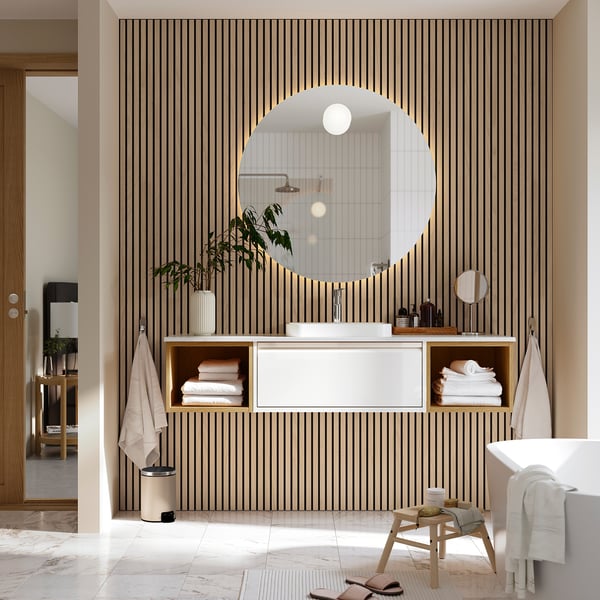 Modern bathroom with floating sink, large mirror, open shelves, plants, and towels.