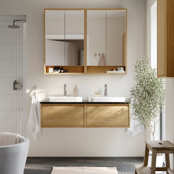 Modern bathroom with oak double vanity, white basins, mirror cabinet, and shower. Light wood, dark counter, minimalist design.
