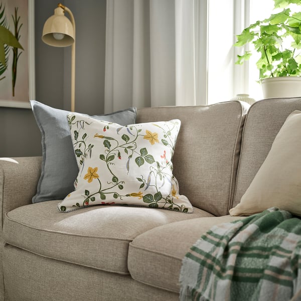 Beige sofa with ÄNGSPALPMAL cushion, blue accent pillow, striped throw, plant, lamp, large window.