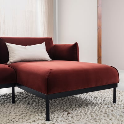 Red velvet sofa with pillows, slim black legs, white rug, large window with sheer curtains.