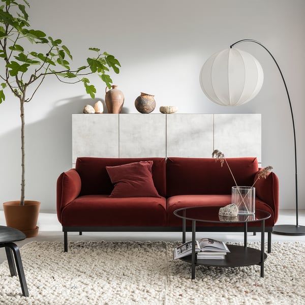 Modern living room with velvet sofa, glass table, rug, lamp, and plant.