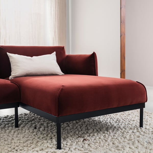 Red modern sofa with metal legs, white pillow, plush rug, near curtain.