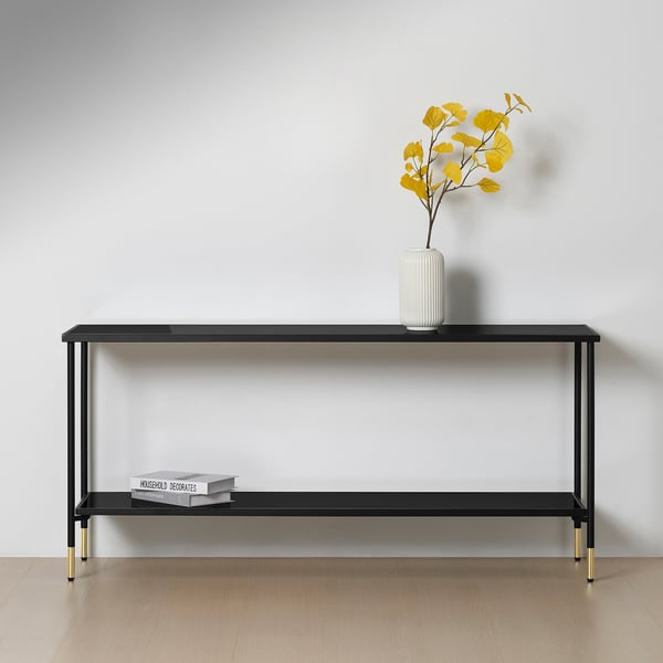 Modern black console table with gold accents and glass top. It holds a vase with yellow flowers and books.