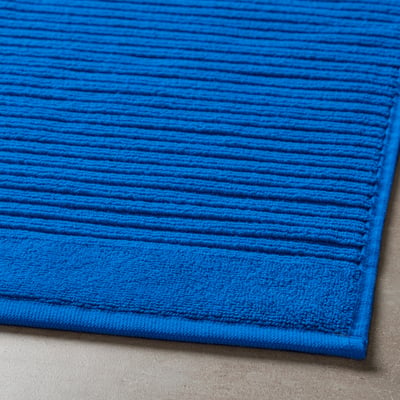 Bright blue, thick cotton bath mat with high absorption, laid on grey floor.