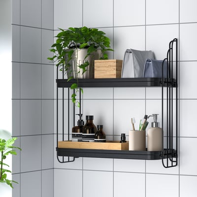 Wall-mounted shelf with two tiers storing bathroom items: bottles, toothbrushes, towels, and a plant in a tiled room.