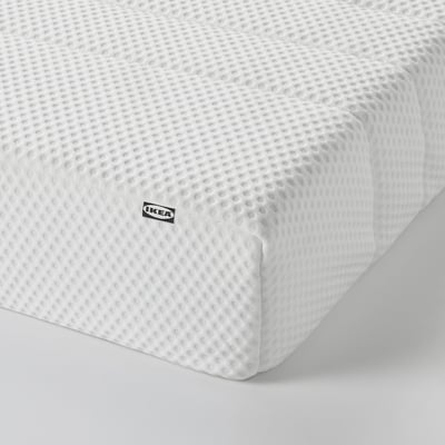 A close-up of a white memory foam mattress with a textured cover, a black IKEA tag visible.