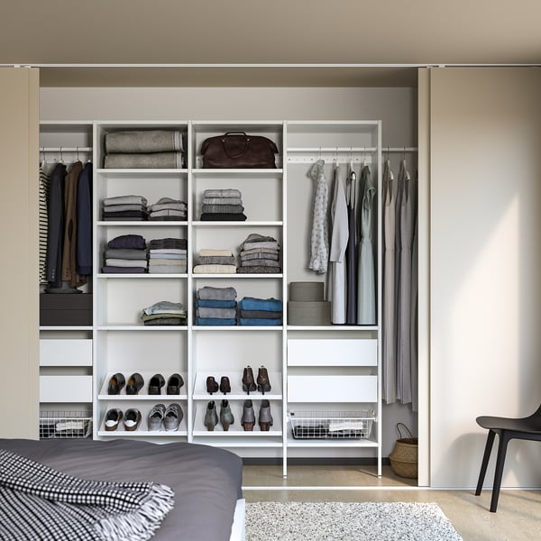 Modern closet with white shelves, drawers, and hanging garments. Grey bed left, black chair right.