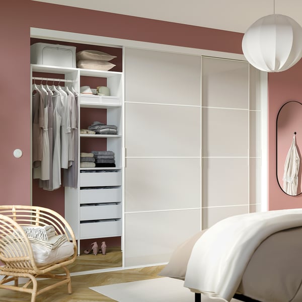 Modern mirrored closet with AURDAL system, organised clothes and shelves, next to bed, lamp, and wicker chair.