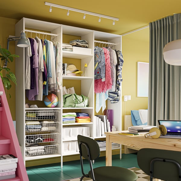 Room with white modular storage, clothes, books, desk, and chair.