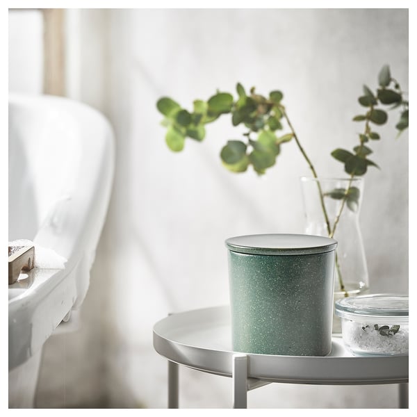 Modern bathroom with white bathtub, grey round table, green speckled candle, clear vase, and fresh plant.
