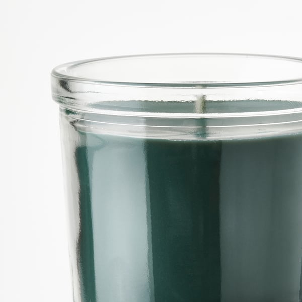 Glass candle close-up; smooth, green wax surface, thin wick, clean edge.
