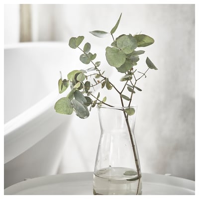 Clear vase with green eucalyptus leaves on white table. Simple, elegant design.