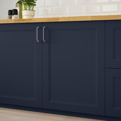 Navy blue kitchen cabinets with silver handles, topped with wooden counter and white tiles.