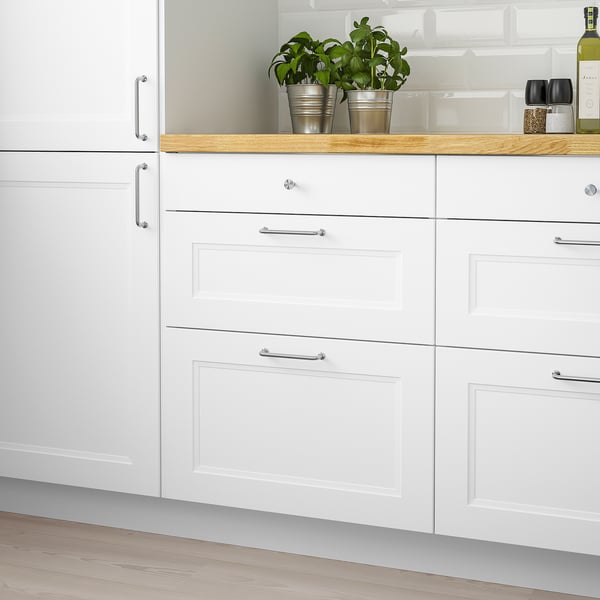 AXSTAD white kitchen drawers, modern, smooth lines, soft close, 25-year guarantee, sleek handles, with potted plants and bottle on countertop.