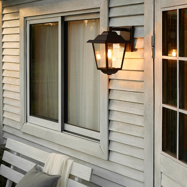 Black wall lantern near windows on grey building.