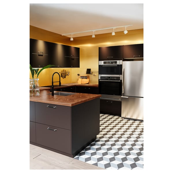 Modern kitchen with black cabinets, geometric tiled floor, stainless steel appliances, wooden countertop, and overhead lighting.