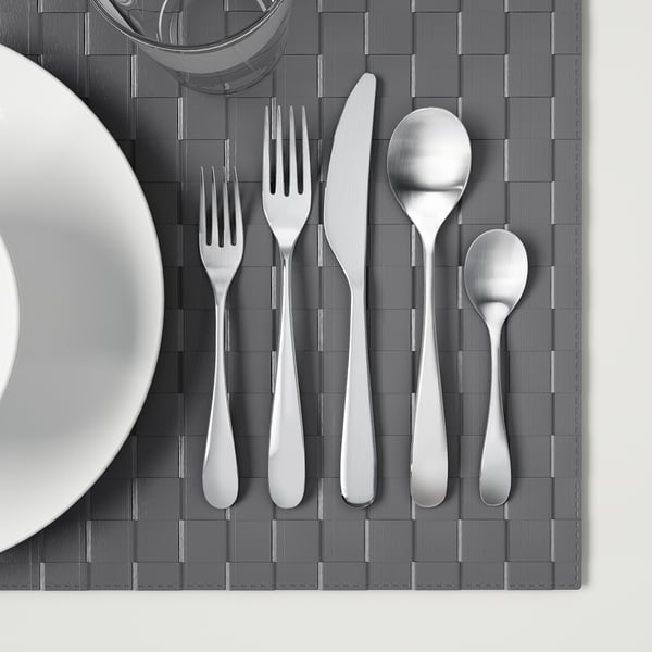 Polished cutlery set on woven placemat. Includes fork, knife, spoon, and teaspoon. Suits various table settings.