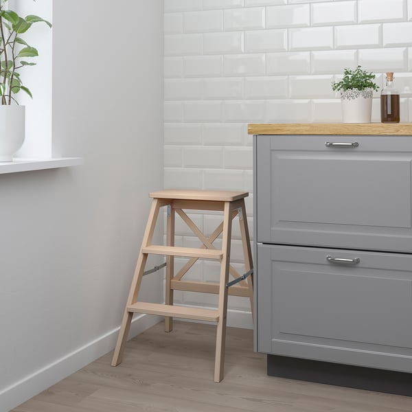 Wooden step ladder, brown, foldable. Leans against kitchen cabinets.