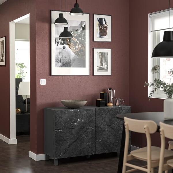 Stylish living space with dark red walls, sleek sideboard, and black pendant lights. Modern decor with framed art and wooden chairs.