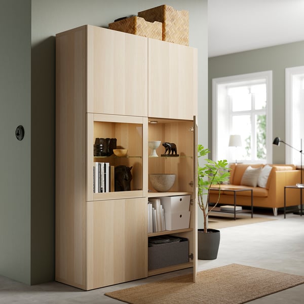 Wooden storage unit with glass doors, displaying decor items and books. One door open shows adjustable shelves and storage boxes.