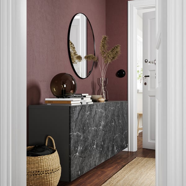 Modern entryway with dark purple wall, black marble console, round mirror, dried flowers, woven basket, and white door.