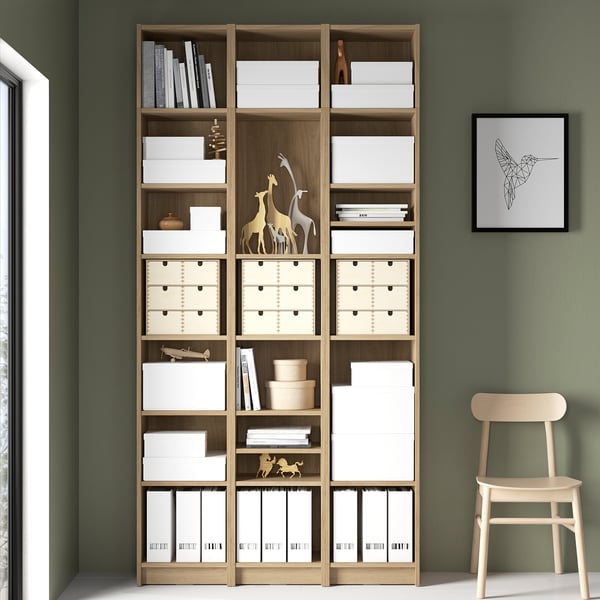 Tall BILLY bookcase with white & wooden storage boxes and decorative items. Set against a green wall.