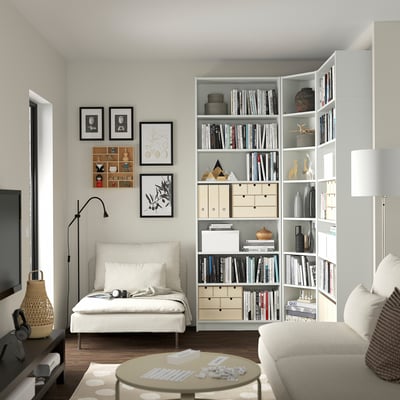 Modern living room with a BILLY bookcase, filled with books and decorative items, beside a white armchair and framed artworks on the wall.