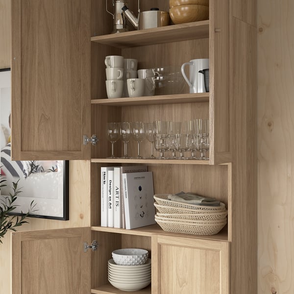 Wooden bookcase with glassware, mugs, books, and bowls neatly organised on shelves.