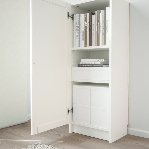 White BILLY bookcase with one door open, displaying shelves with books and magazines, set on wooden floor with white door in background.