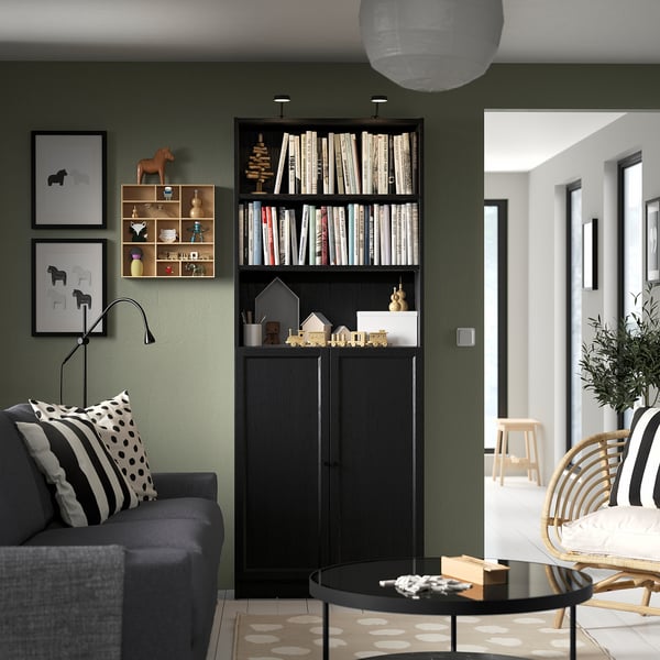 Modern living room with grey sofa, black BILLY bookcase filled with books, decorative items, and prints on olive green wall.