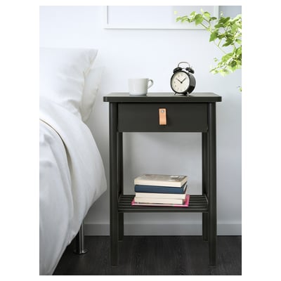 Black wooden bedside table beside a bed with a drawer, clock, mug, and books.
